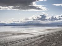 a lone motor cycle is parked on a beach at low tide waterside with mountains in the background