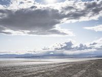 a lone motor cycle is parked on a beach at low tide waterside with mountains in the background