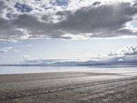 a lone motor cycle is parked on a beach at low tide waterside with mountains in the background