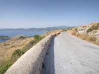 a lone motorcycle parked on a road beside the sea, with a wall separating the road