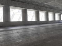 a motorcycle parked under the freeway by an overpass with columns in the background that make it look like a long corridor