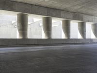 a motorcycle parked under the freeway by an overpass with columns in the background that make it look like a long corridor