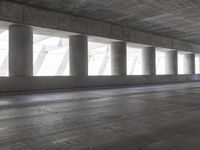 a motorcycle parked under the freeway by an overpass with columns in the background that make it look like a long corridor