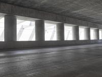 a motorcycle parked under the freeway by an overpass with columns in the background that make it look like a long corridor