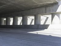 a motorcycle parked under the freeway by an overpass with columns in the background that make it look like a long corridor