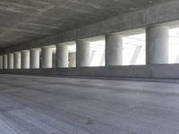 a motorcycle parked under the freeway by an overpass with columns in the background that make it look like a long corridor