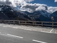 a motorcycle is parked near a mountain road on a sunny day with the snow capped peaks in the distance