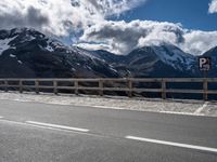 a motorcycle is parked near a mountain road on a sunny day with the snow capped peaks in the distance