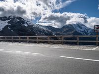 a motorcycle is parked near a mountain road on a sunny day with the snow capped peaks in the distance