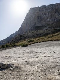 a brown motorcycle parked in the sand on a mountain top with a sun behind it