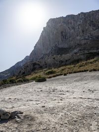 a brown motorcycle parked in the sand on a mountain top with a sun behind it