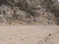 a lone motorcycle is parked along side of the mountainside on dirt road in the desert