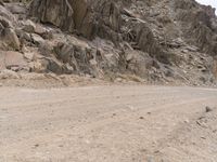 a lone motorcycle is parked along side of the mountainside on dirt road in the desert