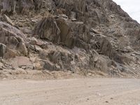 a lone motorcycle is parked along side of the mountainside on dirt road in the desert