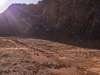 a motorcycle is parked in front of some mountains and rocks while the sun shines on it