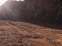 a motorcycle is parked in front of some mountains and rocks while the sun shines on it