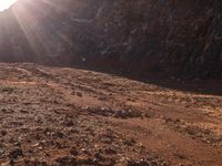 a motorcycle is parked in front of some mountains and rocks while the sun shines on it