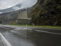 a lone motorcycle is parked on the side of a wet road in front of a mountain