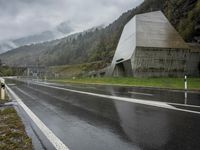 a lone motorcycle is parked on the side of a wet road in front of a mountain