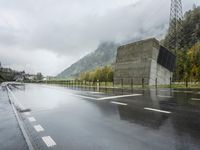 a lone motorcycle is parked on the side of a wet road in front of a mountain