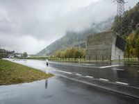 a lone motorcycle is parked on the side of a wet road in front of a mountain