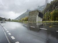 a lone motorcycle is parked on the side of a wet road in front of a mountain