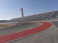 a person rides on a motorcycle on the track in front of an empty stadium, near the water