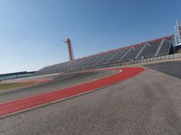a person rides on a motorcycle on the track in front of an empty stadium, near the water