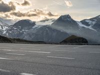 a person riding a motorcycle on the street near a mountain range with snow covered mountains in the background