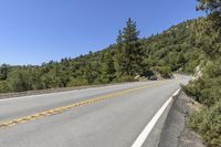 a motorcycle that is driving down a road by the mountains'side with pine trees