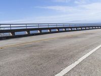 a man riding a motorcycle over a bridge with mountains in the background under a bright blue sky