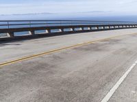 a man riding a motorcycle over a bridge with mountains in the background under a bright blue sky