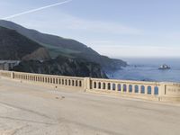 a man riding a motorcycle next to a long bridge over water with cliffs in the distance