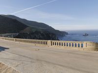 a man riding a motorcycle next to a long bridge over water with cliffs in the distance