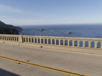 a man riding a motorcycle next to a long bridge over water with cliffs in the distance