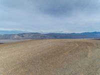 a person is on a motorcycle in the middle of a dirt field near mountains with a blue sky