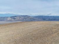 a person is on a motorcycle in the middle of a dirt field near mountains with a blue sky