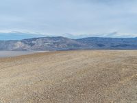 a person is on a motorcycle in the middle of a dirt field near mountains with a blue sky