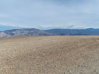 a person is on a motorcycle in the middle of a dirt field near mountains with a blue sky