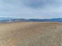 a person is on a motorcycle in the middle of a dirt field near mountains with a blue sky