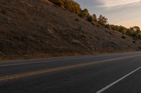 a person riding a motorcycle down the middle of an empty road at dusk with hills in background