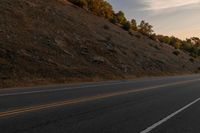 a person riding a motorcycle down the middle of an empty road at dusk with hills in background