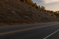 a person riding a motorcycle down the middle of an empty road at dusk with hills in background