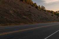 a person riding a motorcycle down the middle of an empty road at dusk with hills in background