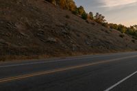 a person riding a motorcycle down the middle of an empty road at dusk with hills in background