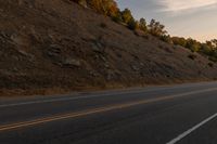 a person riding a motorcycle down the middle of an empty road at dusk with hills in background