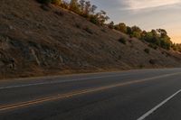 a person riding a motorcycle down the middle of an empty road at dusk with hills in background