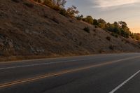 a person riding a motorcycle down the middle of an empty road at dusk with hills in background