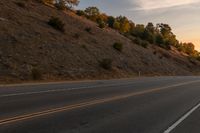 a person riding a motorcycle down the middle of an empty road at dusk with hills in background