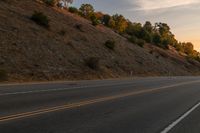 a person riding a motorcycle down the middle of an empty road at dusk with hills in background